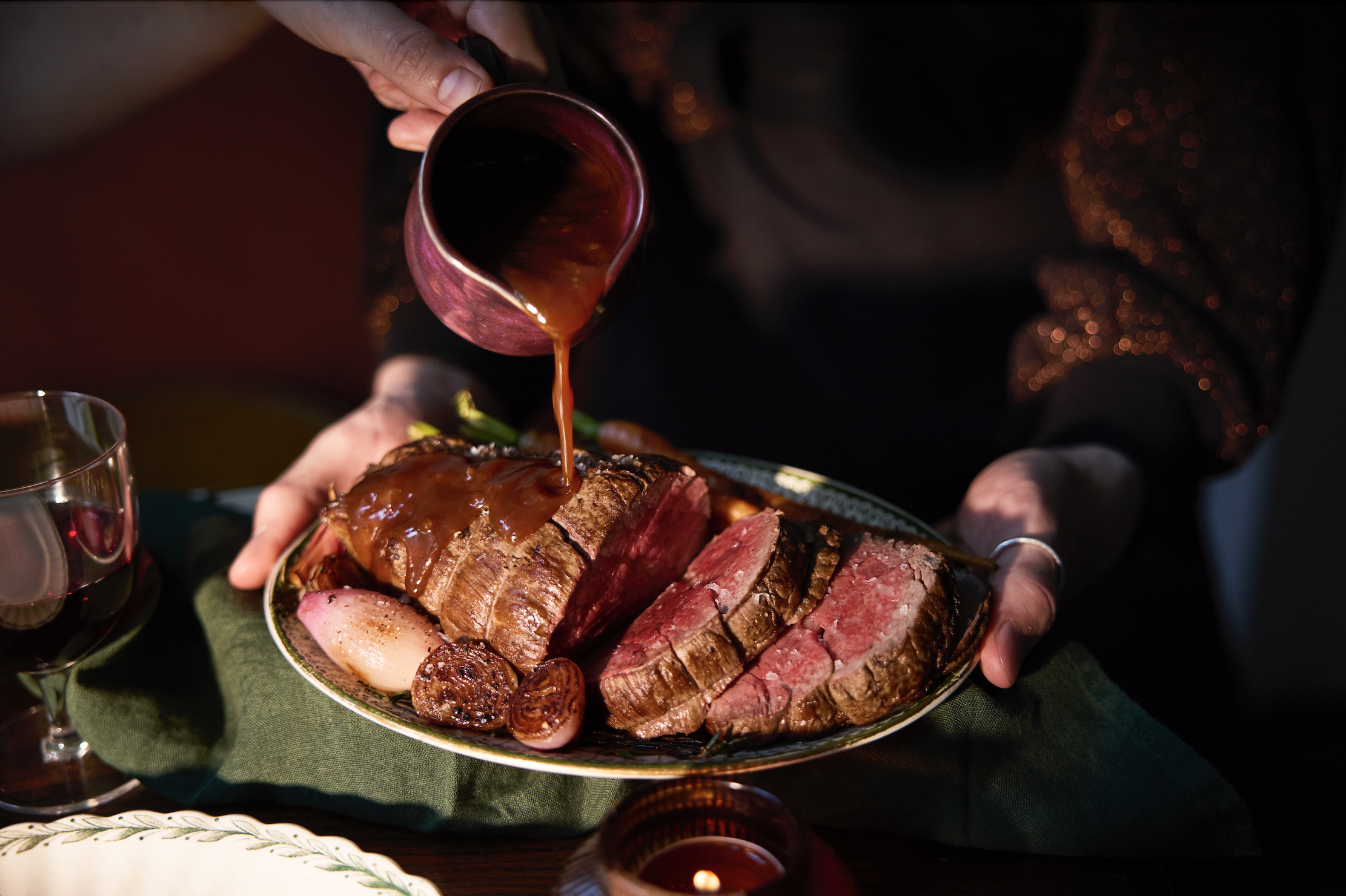 Someone holds a plate of thickly sliced, rare fillet beef with a third hand pouring over gravy