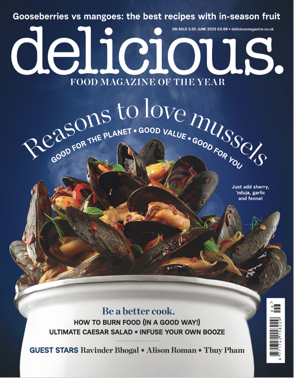 Cover of Delicious magazine featuring a bowl of cooked mussels with herbs and seasonings, against a blue background.