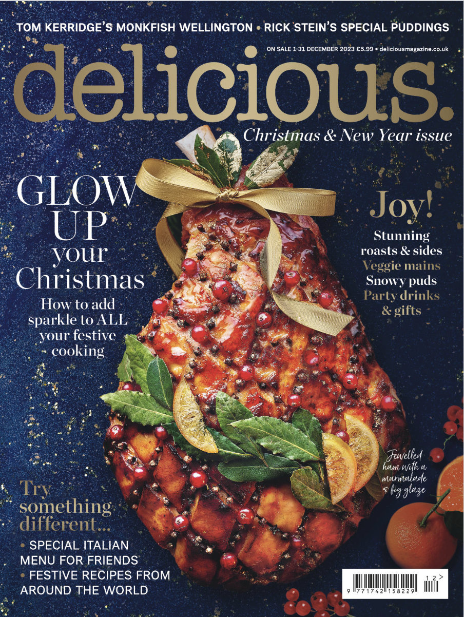 Decorated cooked ham with herbs, citrus slices, and berries on the cover of a delicious magazine Christmas issue.