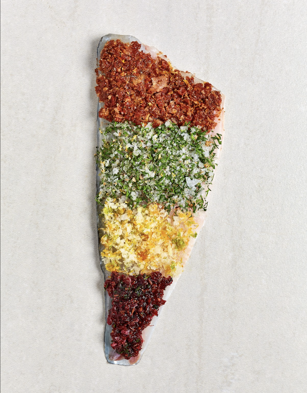 A large fish fillet topped with four different colorful, textured rubs or seasonings arranged in horizontal bands.