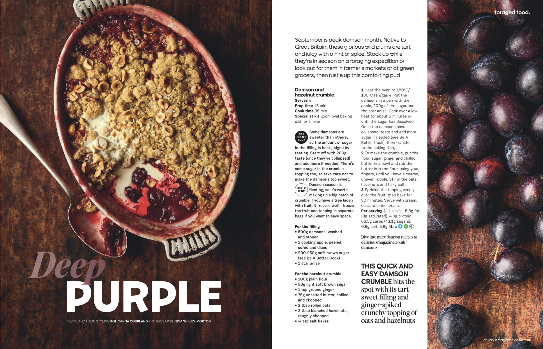 A baked dish of Damson and hazelnut crumble with a red fruit filling, served in a red ceramic dish, topped with chopped hazelnuts and a crumbly streusel. Beside the dish is a spoon with some filling on it. The photograph is on a wooden surface. There