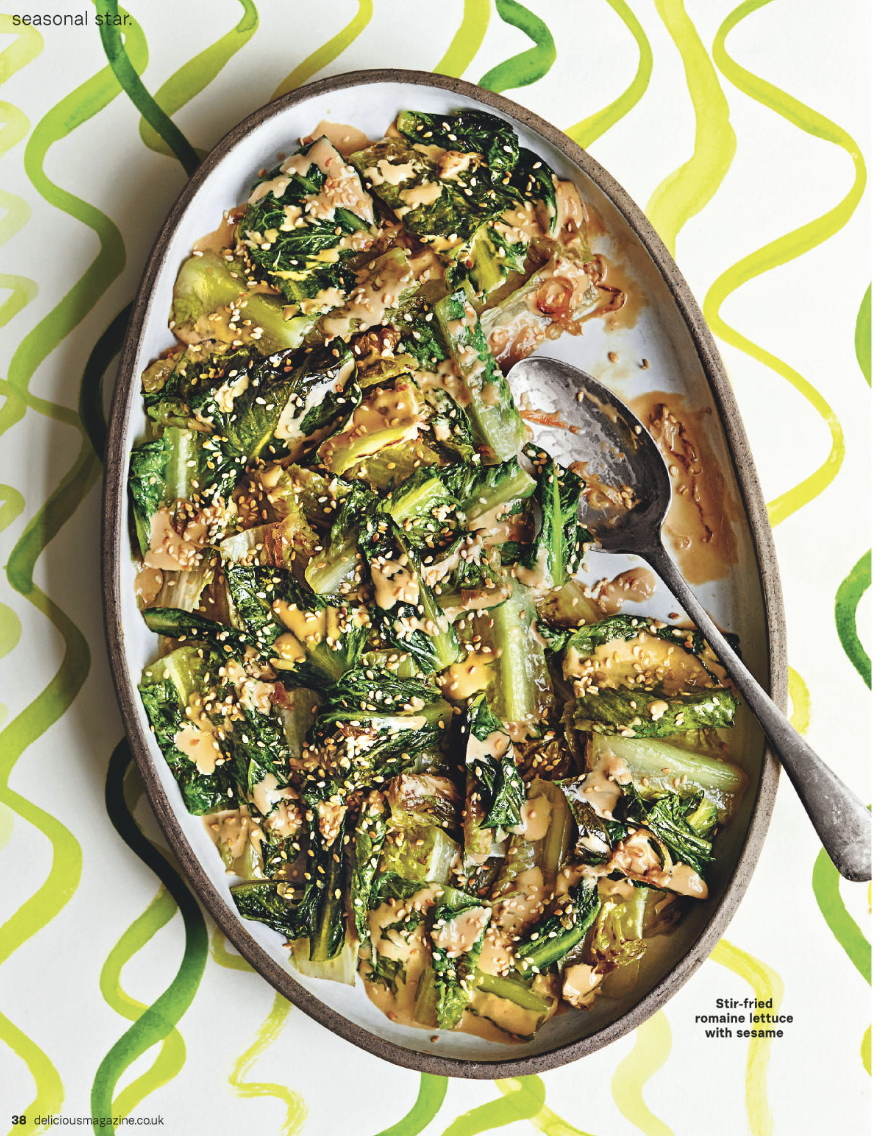 Stir-fried romaine lettuce with sesame seeds on a white oval dish with a spoon, on a decorative green and yellow patterned tablecloth.