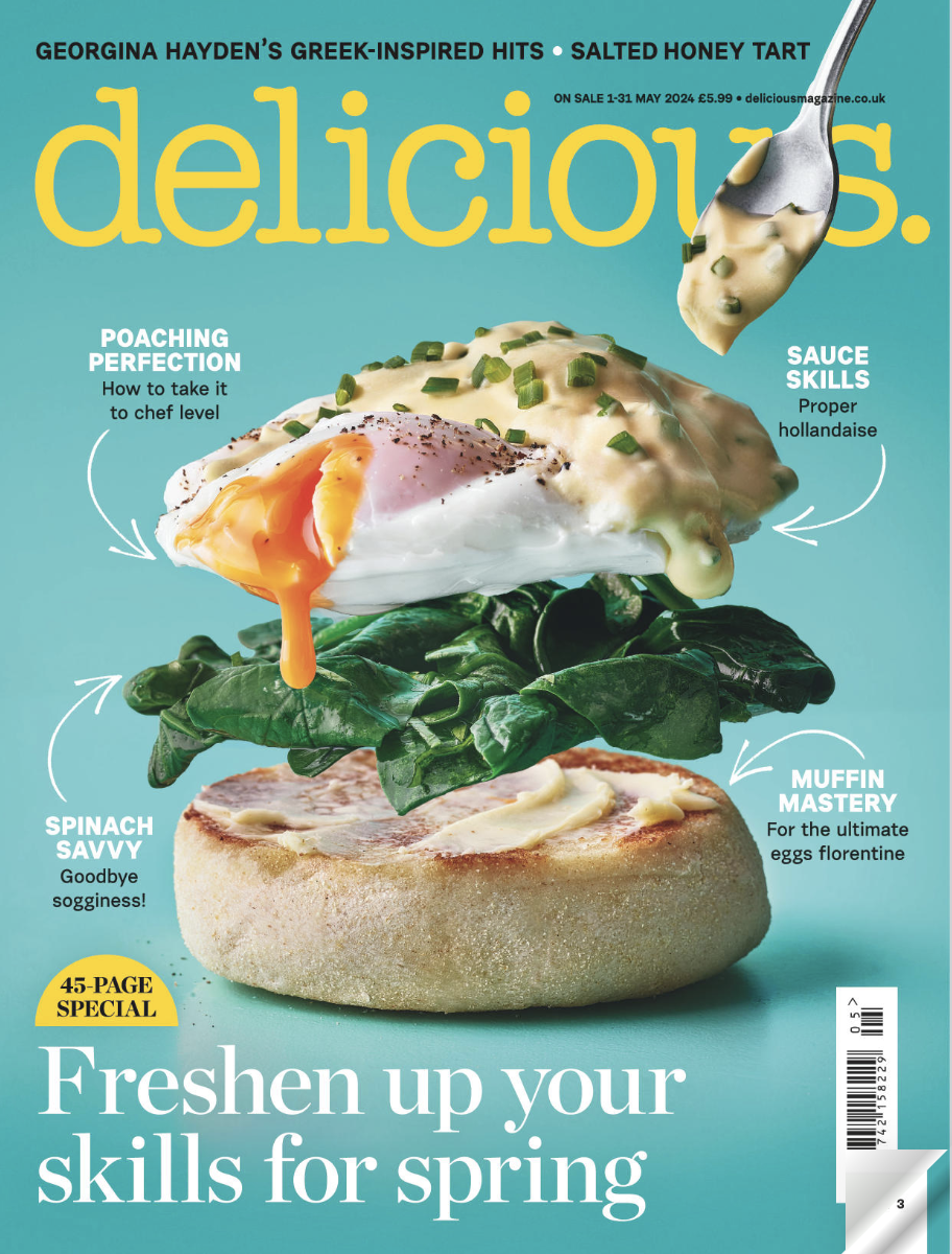 A magazine cover titled 'delicious' featuring a layered food dish with a toasted bun at the bottom, spinach leaves, a poached egg, and a creamy sauce topped with chopped green herbs, with descriptive labels highlighting the ingredients and cooking ti