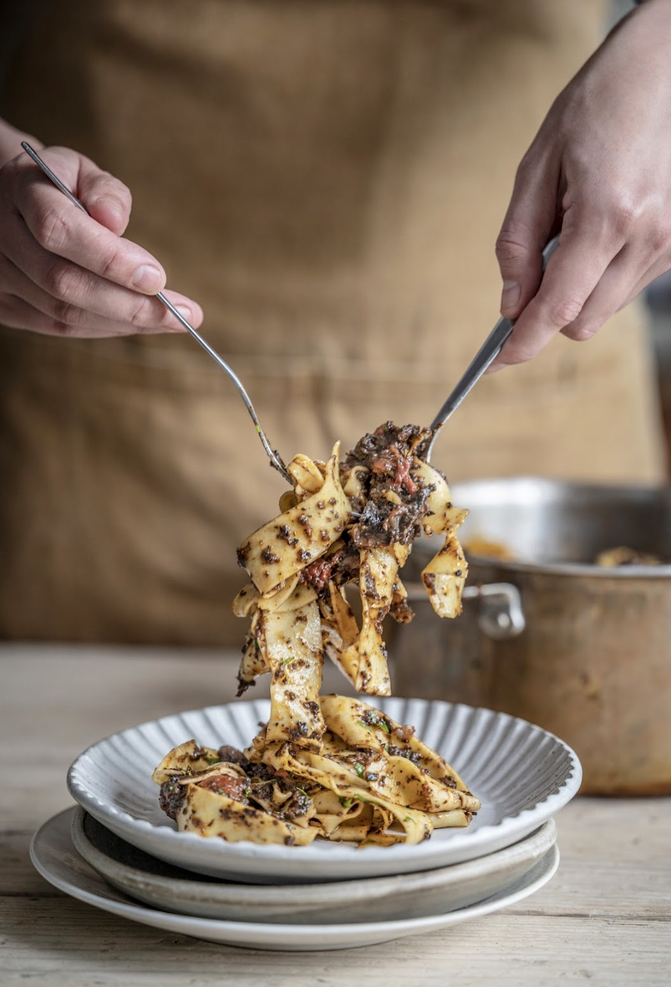 Person serving cooked pasta with beef and sauce onto a plate with two knives.