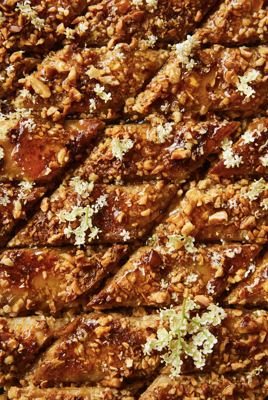 Close-up of sliced dessert topped with chopped nuts and small white edible flowers.