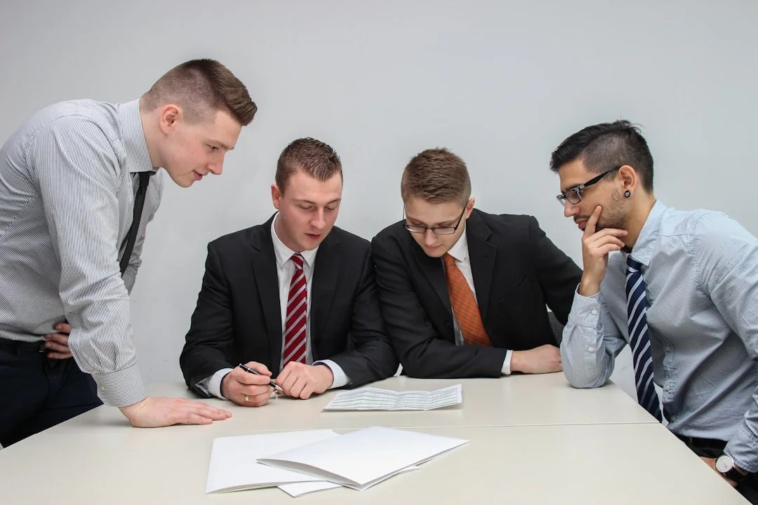 Five young men in business attire gathered around a table, looking at documents and discussing.
