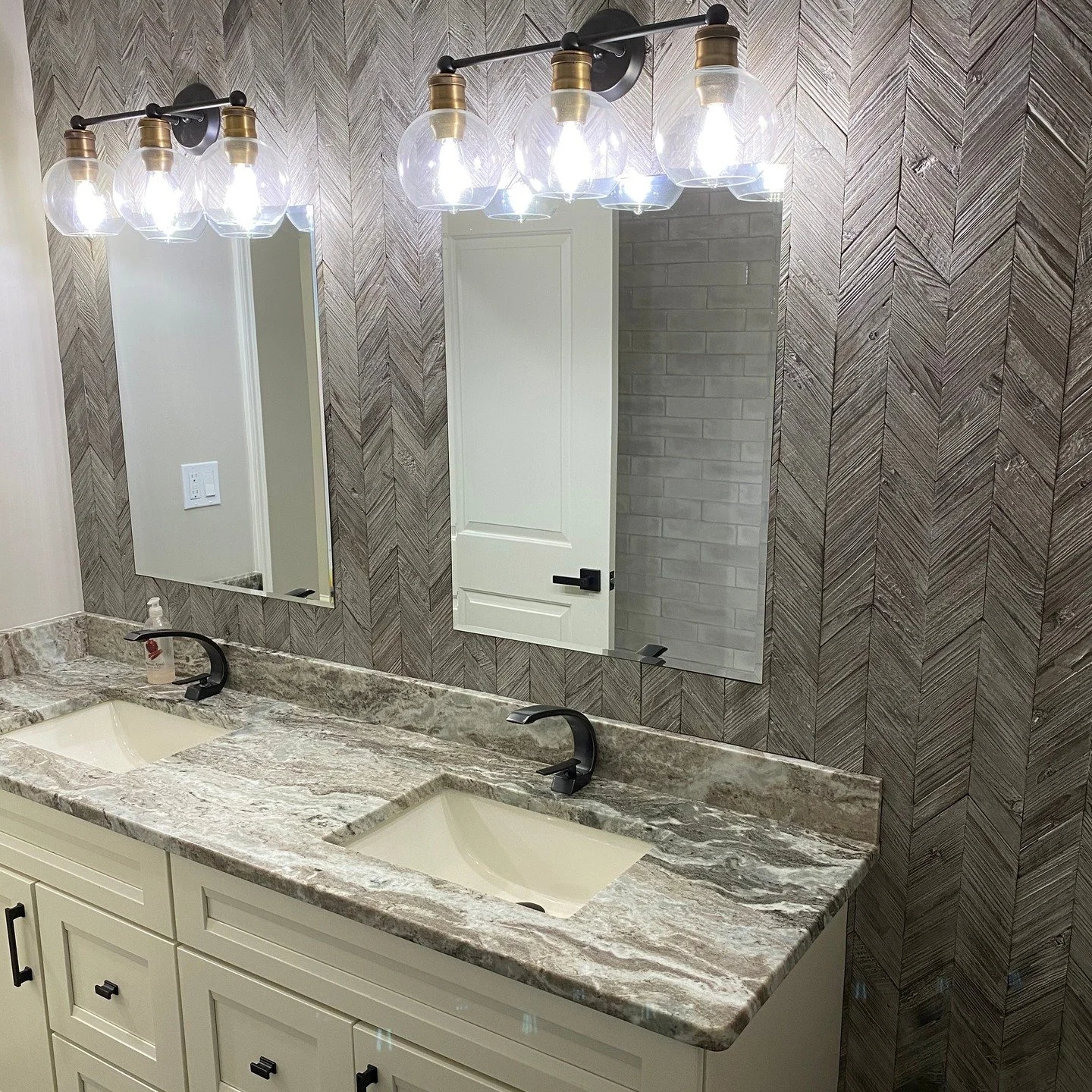 Black herringbone floor, chevron feature wall, creamy double vanity with stone tops, and a glossy subway surround with a rain head. Matte-black fixtures pull it all together.

Serving St. Pete / Tampa Bay&mdash;want yours next? DM &ldquo;BATH.&rdquo;