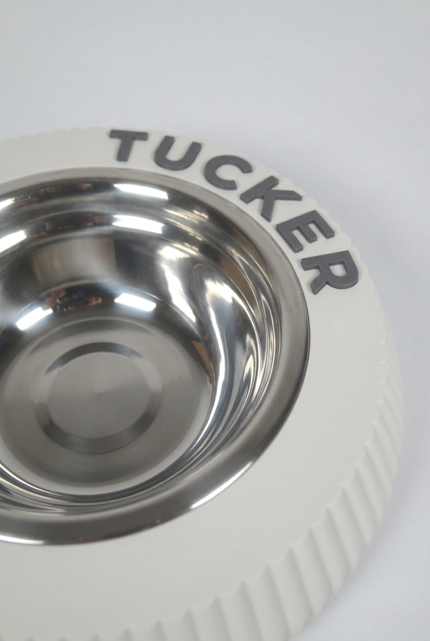 Close view of the rim of a Bone White KAZE pet bowl, the name TUCKER in raised dark grey letters beside the stainless insert.