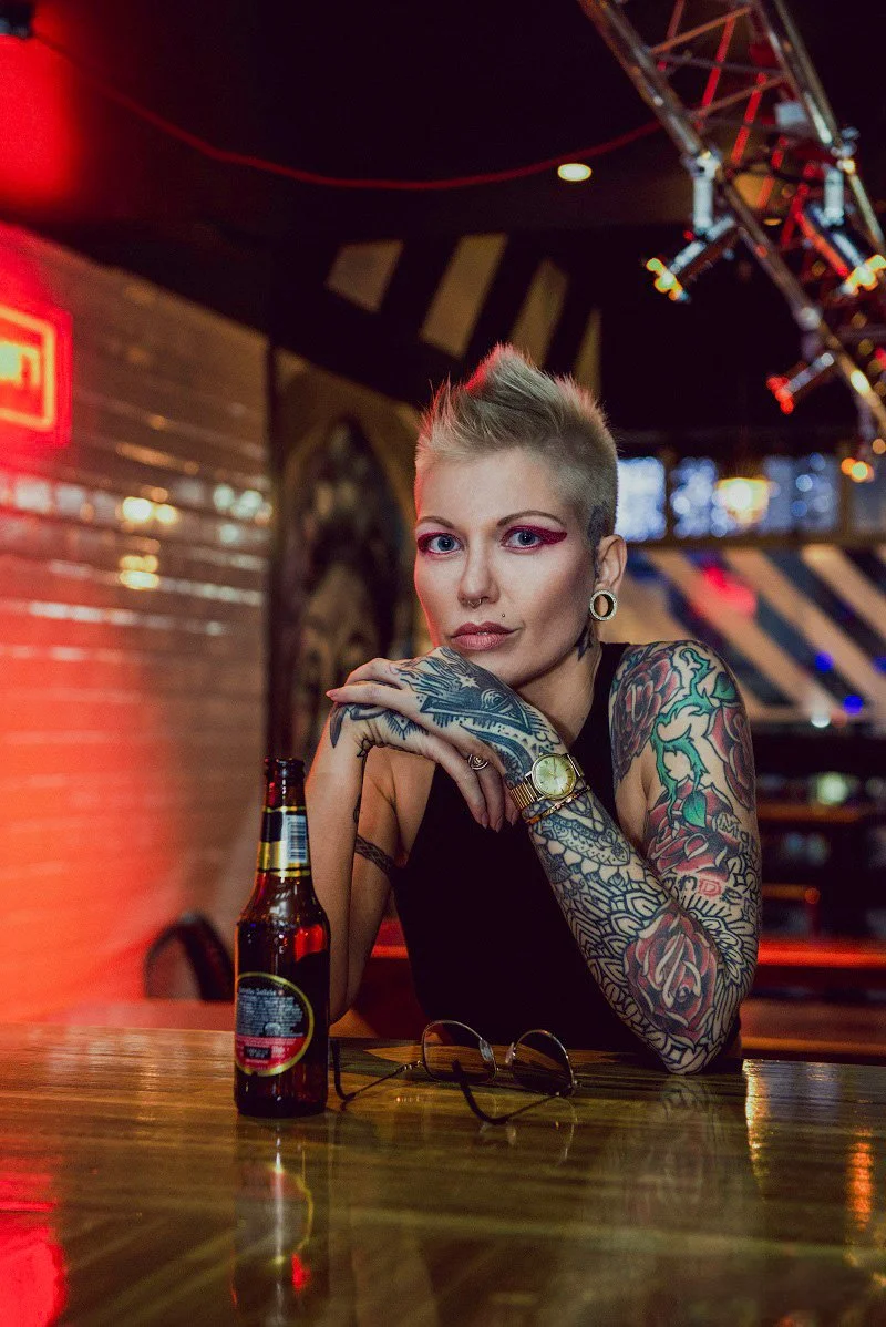 tattooed woman portrait. Izabela Bartnicka Photography, portrait photography, photographer Amsterdam, female photography, fashion, portrait, beautiful blond woman, with tattoos, colorful lights, restaurant