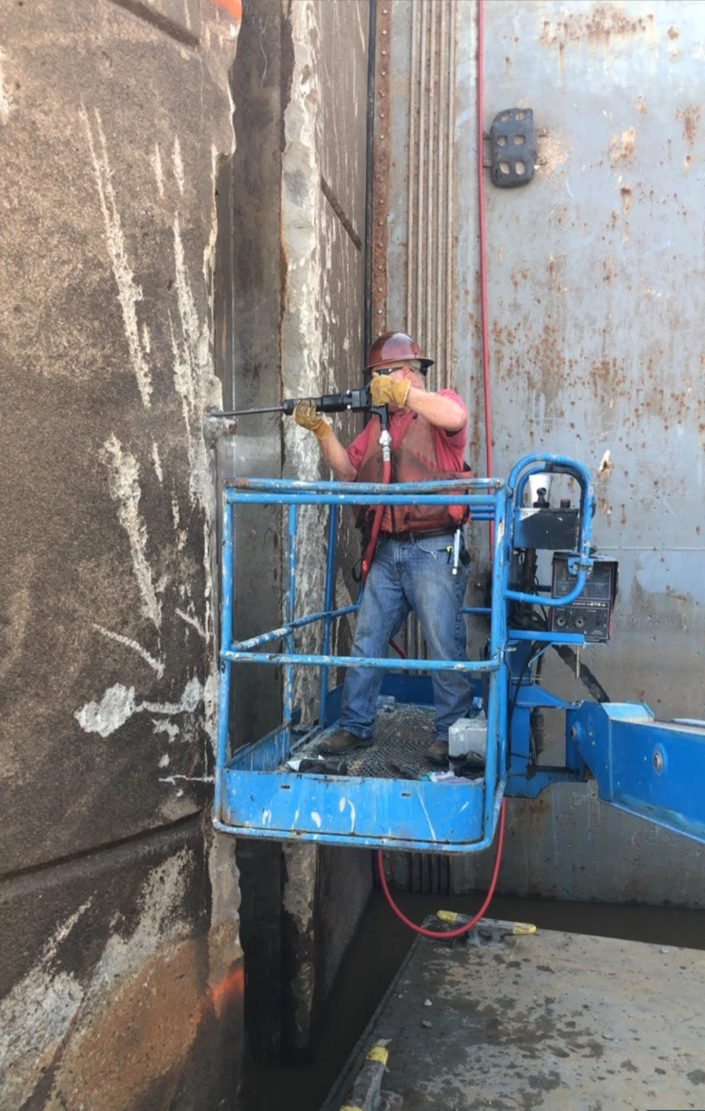 Worker wearing a helmet and gloves operating a drilling or demolition machine on a construction site