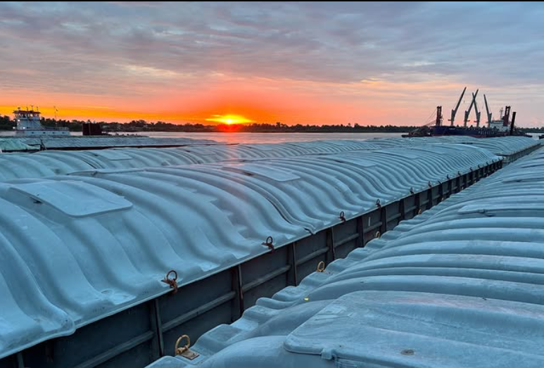 Ice-covered cargo ships docked on a river during sunset.