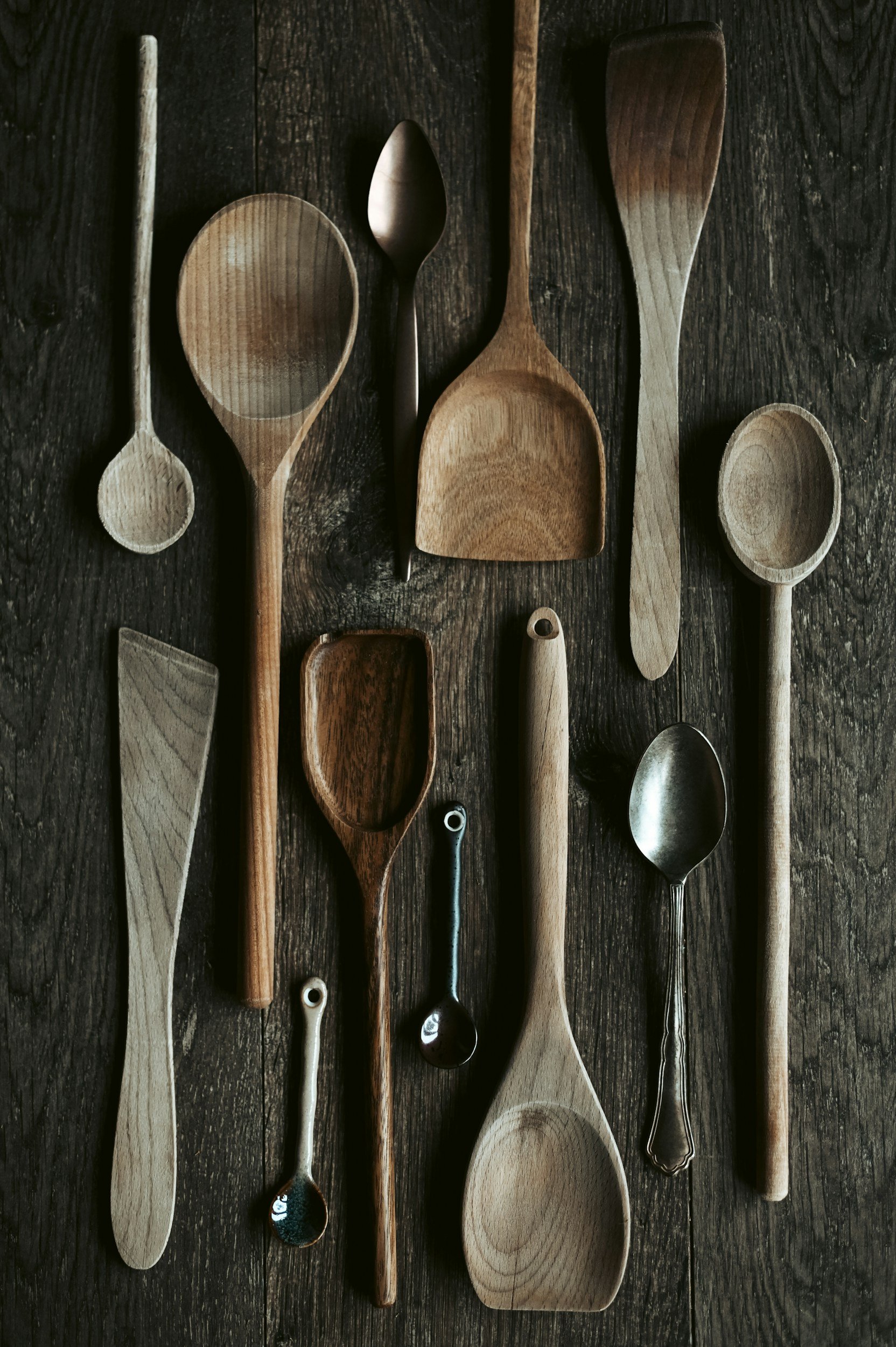 Collection of wooden and metal spoons and utensils on a dark wooden surface.