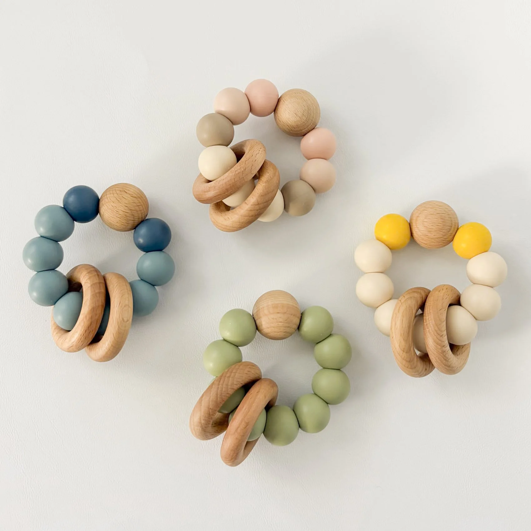 Four colorful baby teething rings made of wooden and silicone beads, arranged on a white surface.