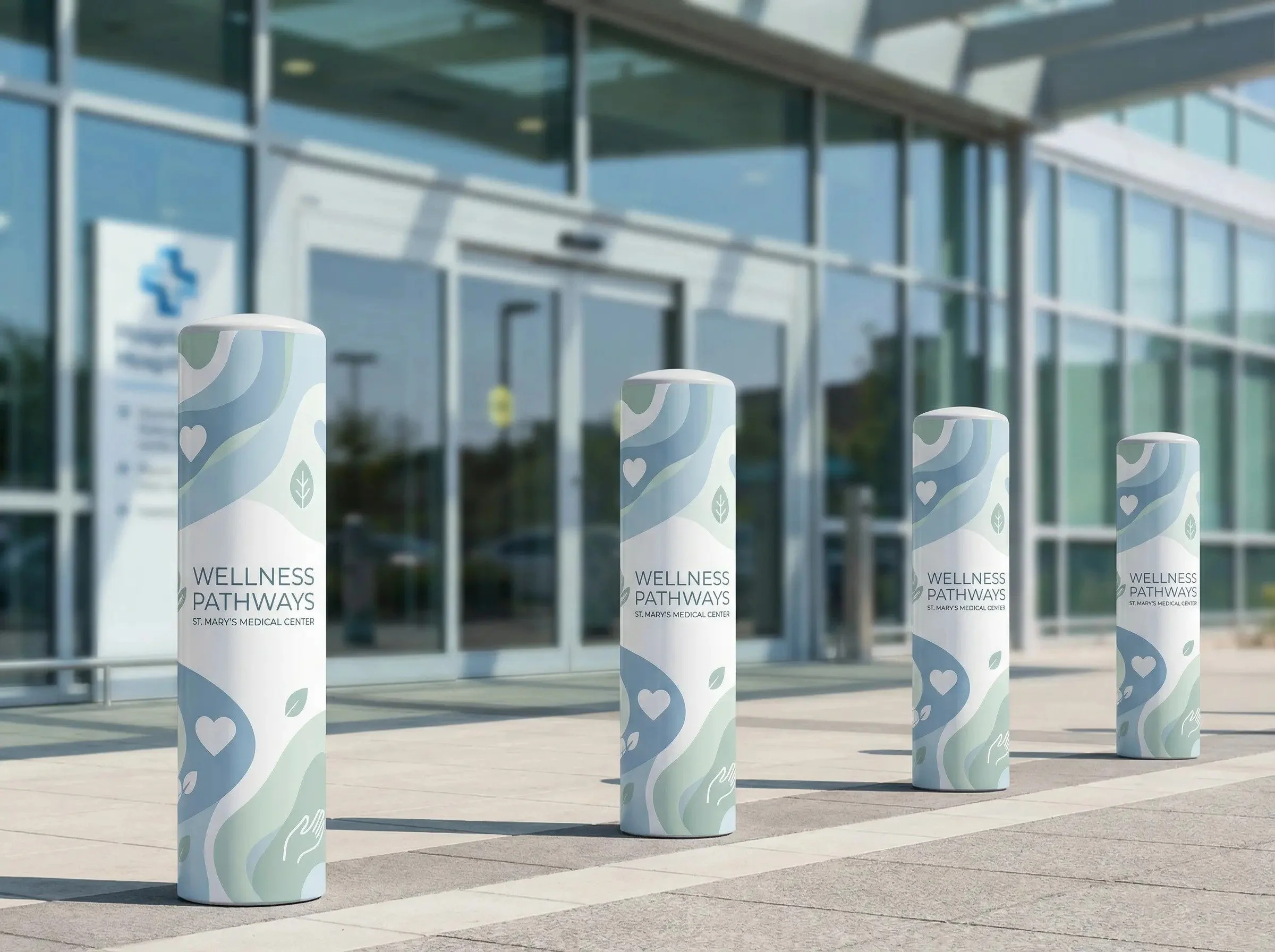 Four cylindrical pillars outside a modern medical center building with glass windows, labeled 'Wellness Pathways, St. Mary's Medical Center.'