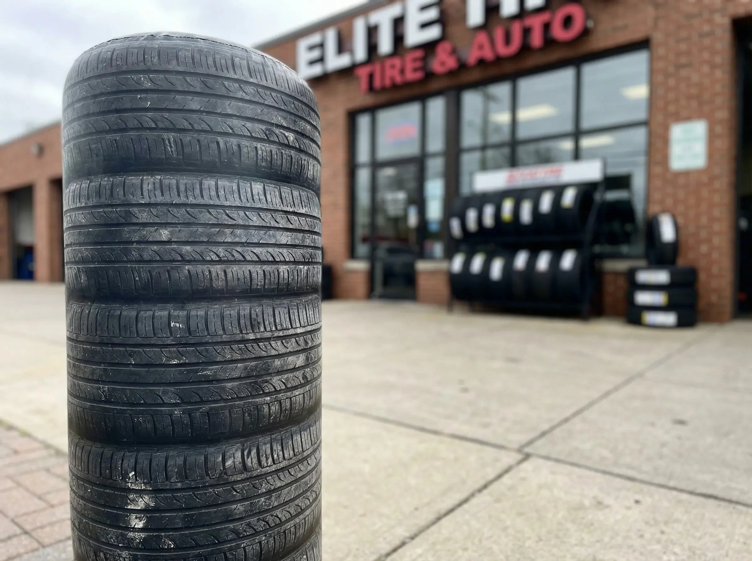 Stack of used tires outside of a tire and auto shop with a sign that reads "Elite Tire & Auto".