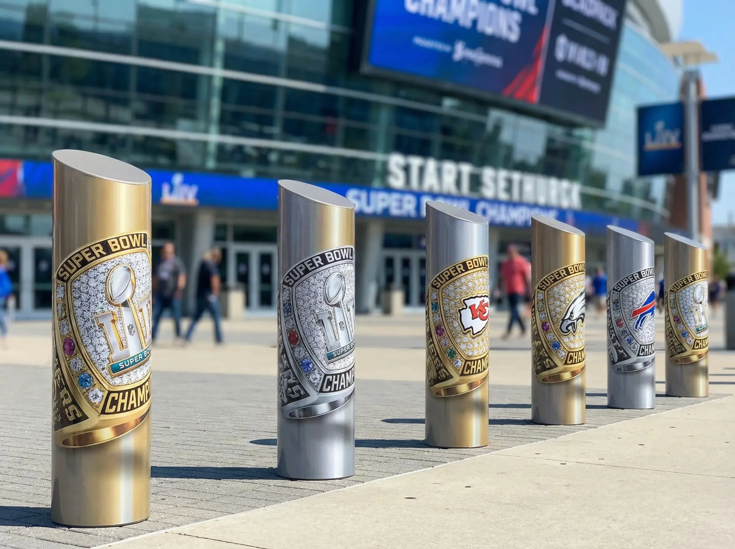 Super Bowl championship trophies lined up outside a stadium with large digital screens showing Super Bowl logos and teams.