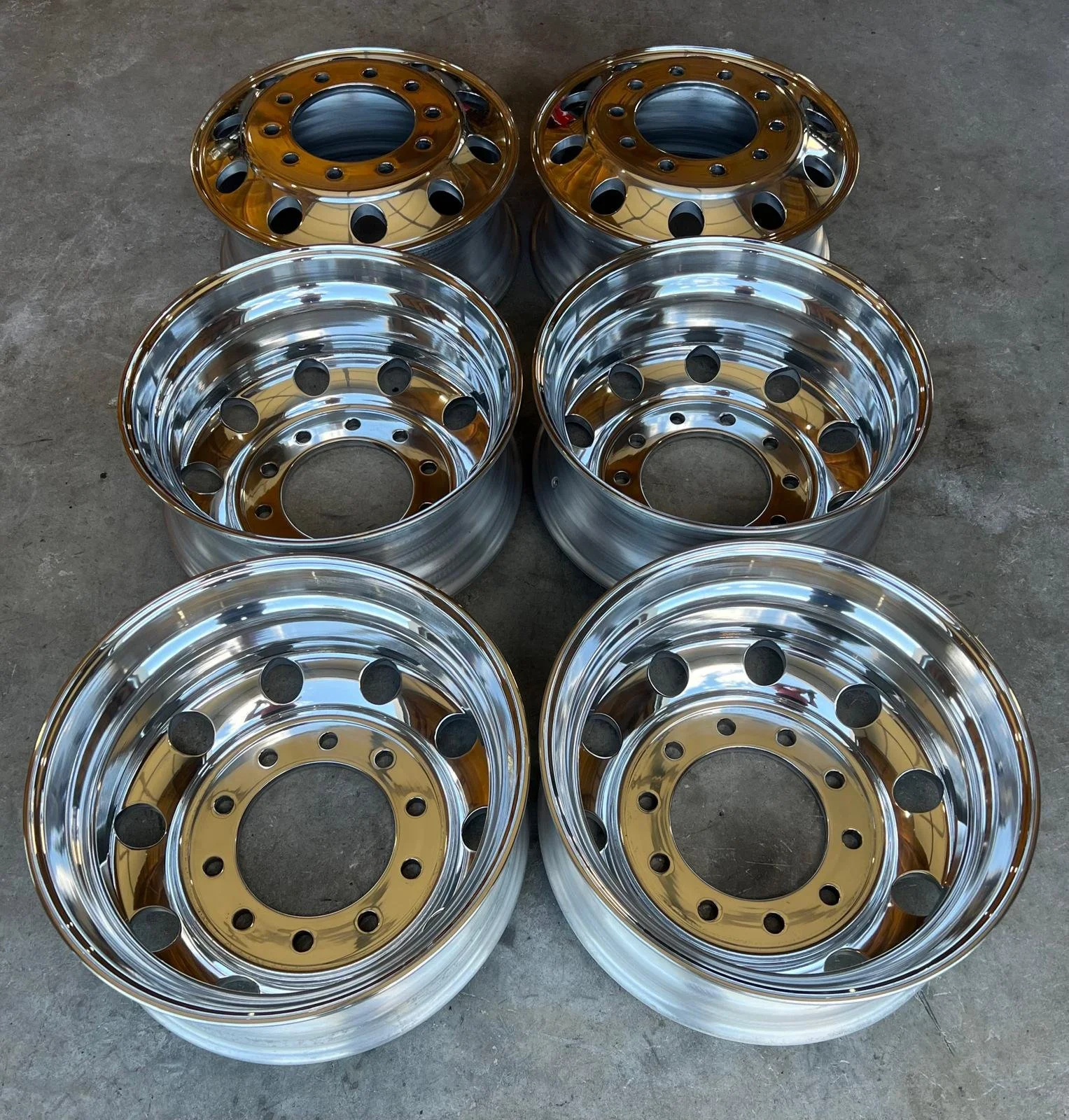 Six shiny alloy wheels stacked in a pyramid formation on a concrete floor.