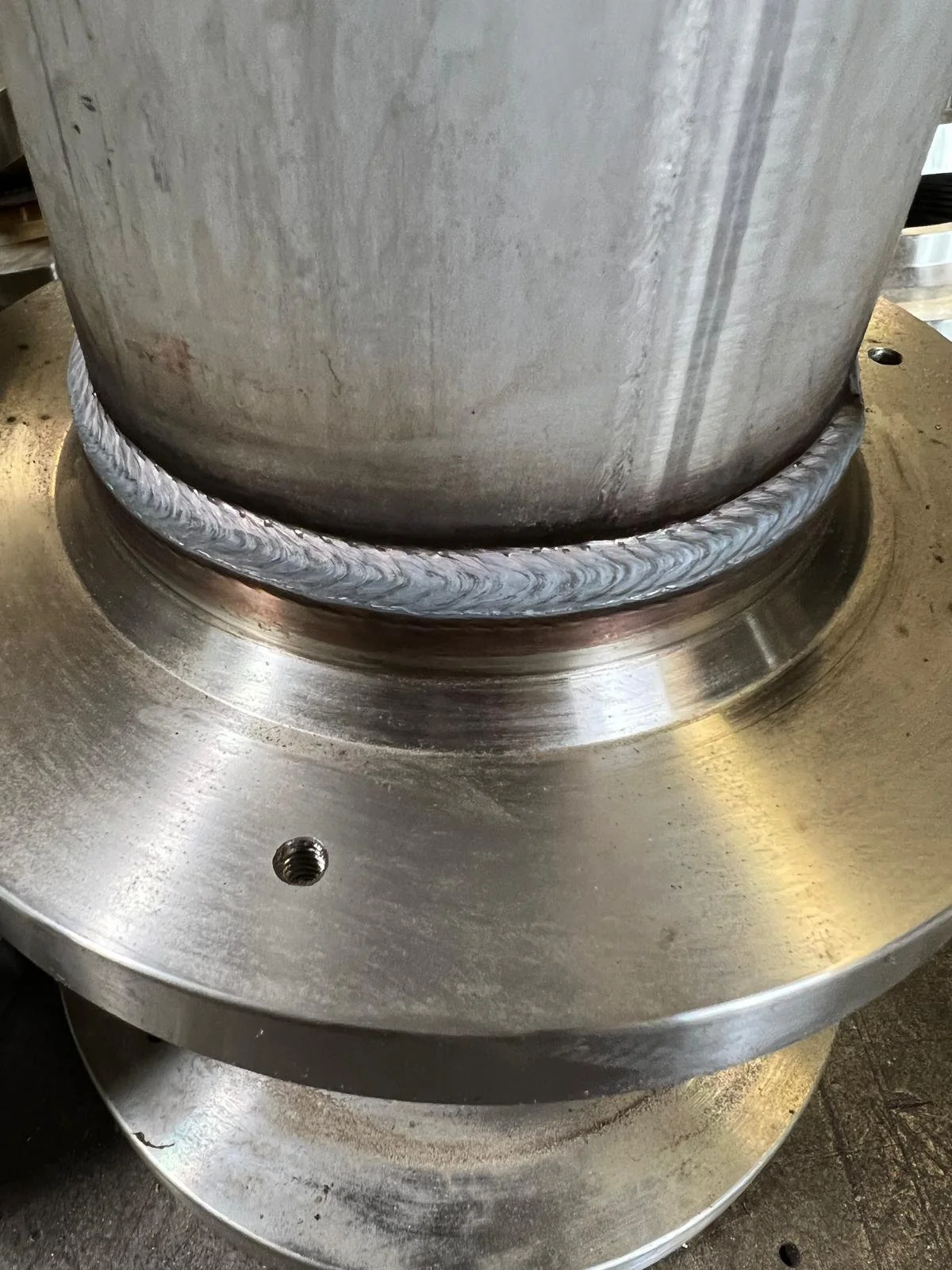 Close-up of a large metal welding repair around a cylindrical metal piece.