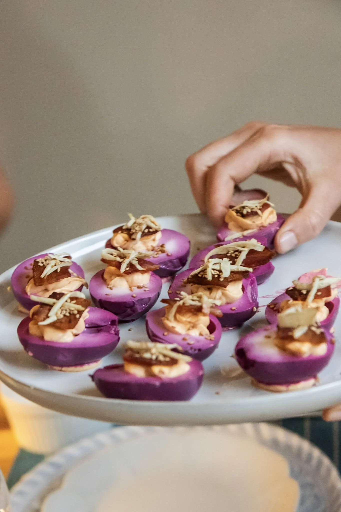 Person holding a white plate with purple deviled eggs topped with shredded cheese and garnishes.