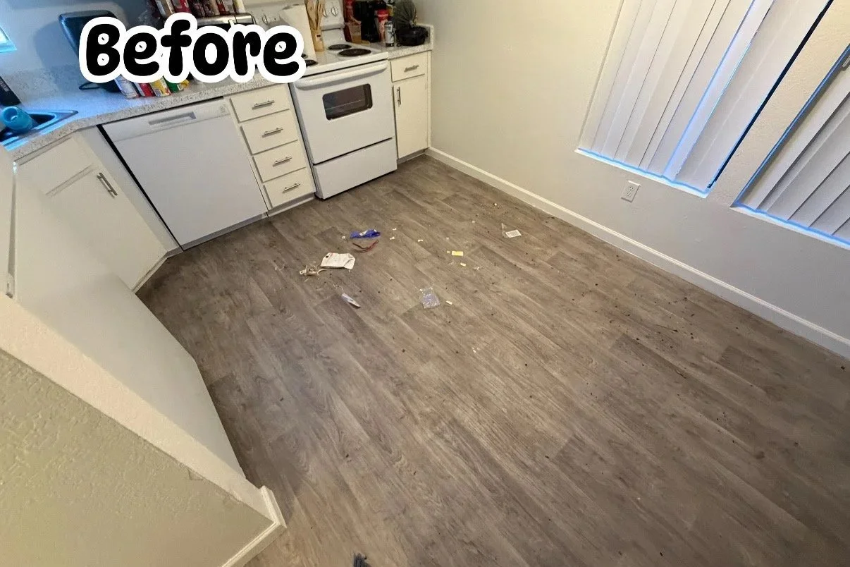 Empty kitchen with scattered trash and debris on the floor, white cabinets, and a window with vertical blinds.