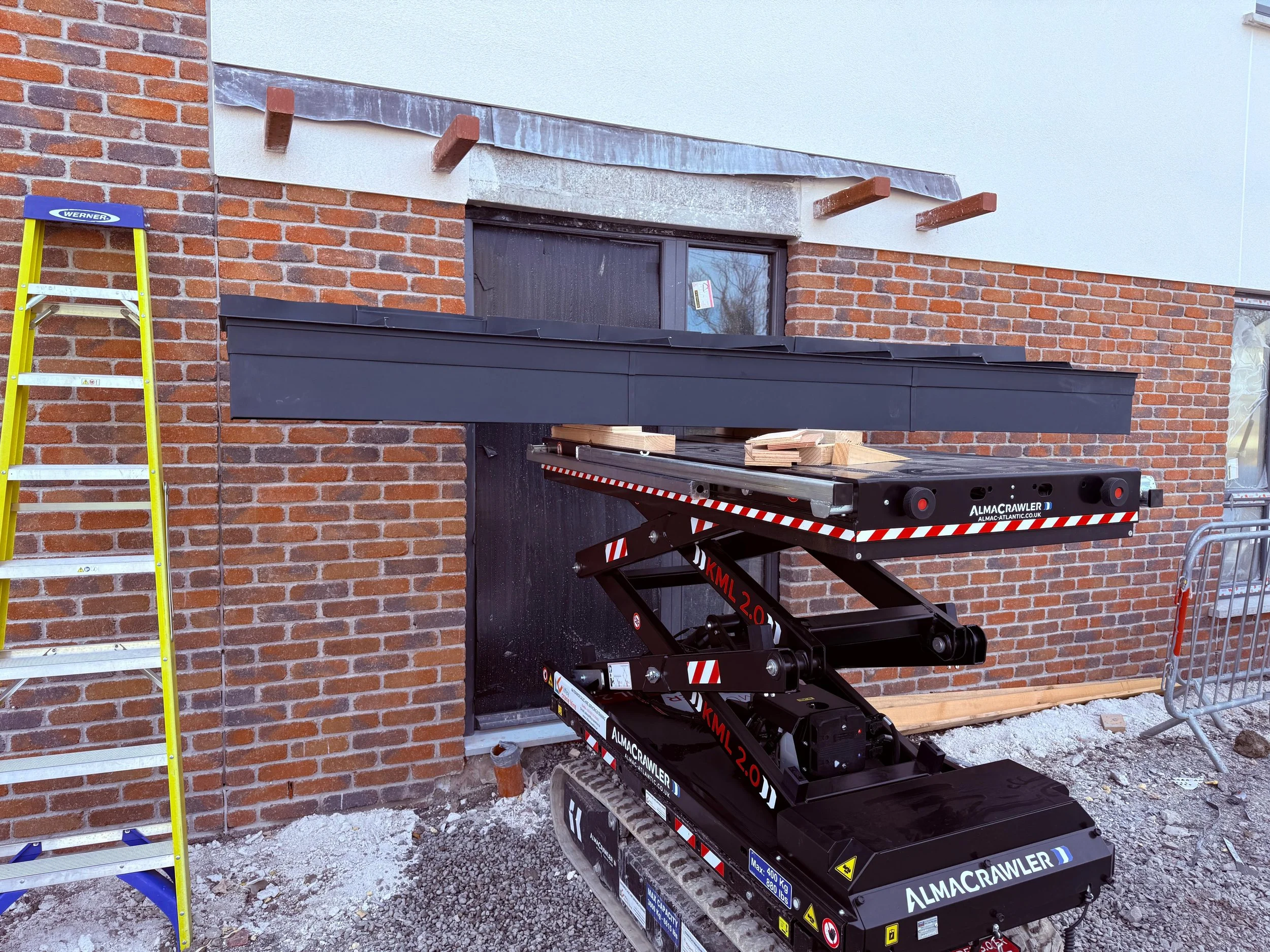 Construction scene with a tracked scissor lift elevated at a building exterior, a yellow ladder on the left, and construction materials and barriers on the ground.