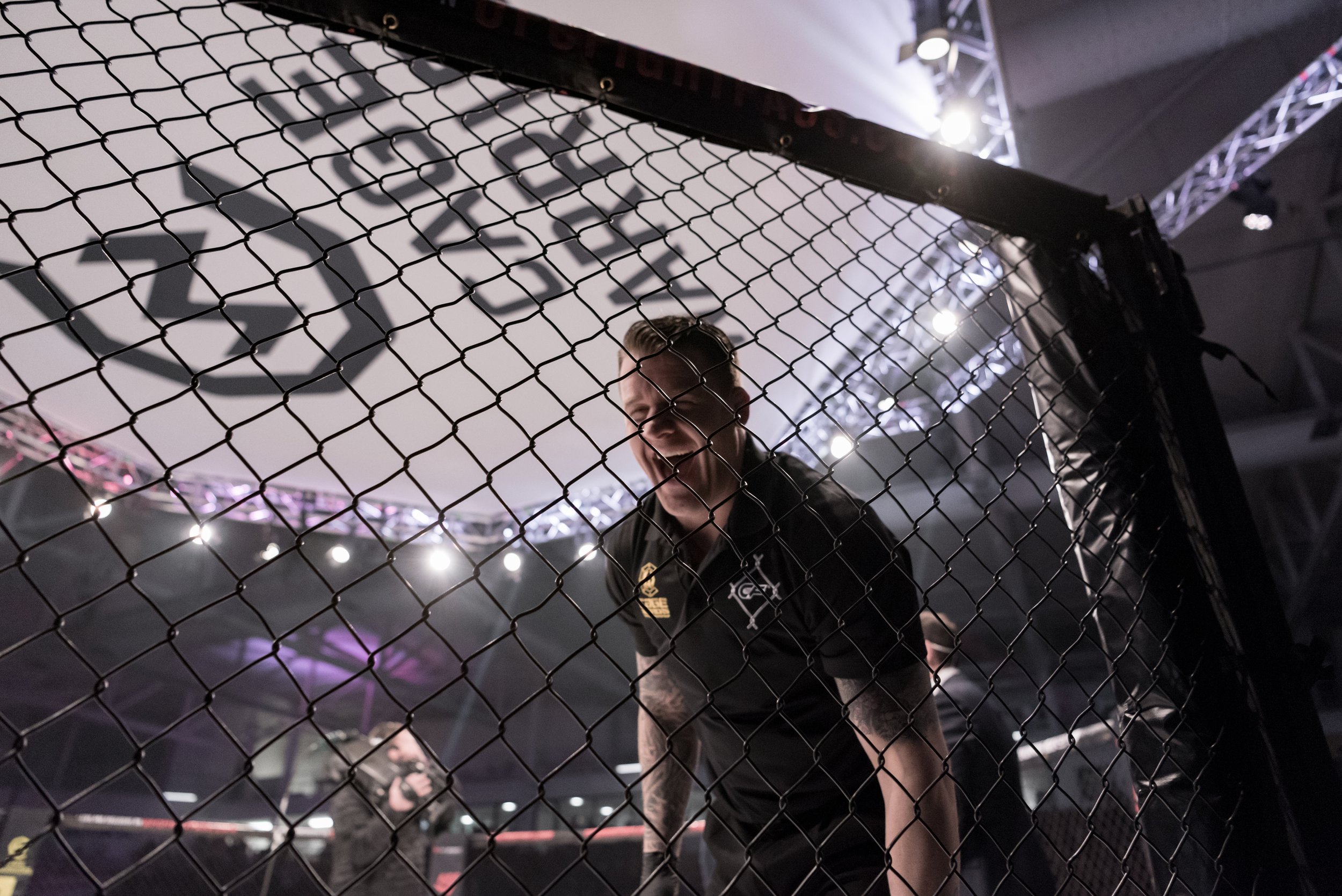 Marc Goddard laughing at the Raspberry Ape (Daniel Strauss) through the cage at Cagewarriors 100 in Cardiff