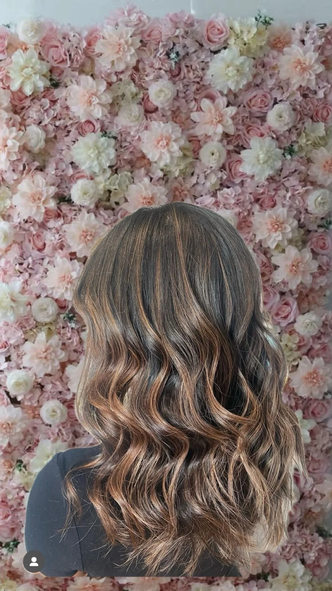 A person's hair styled in loose, wavy curls with brown and caramel highlights against a pink and white floral background.