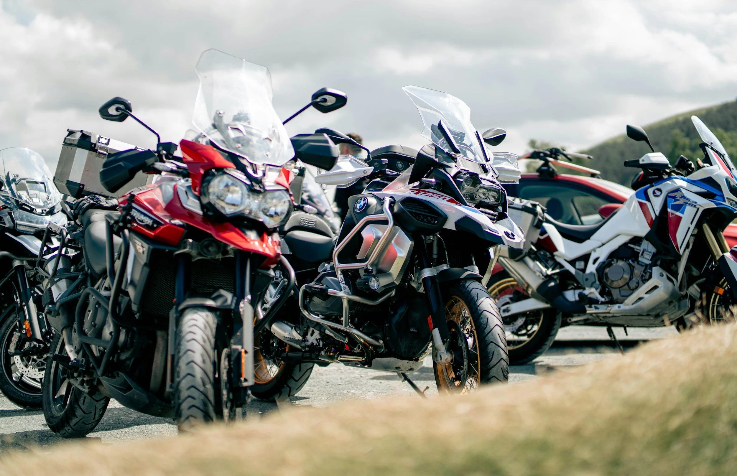 A lineup of heavy adventure motorcycles equipped with windscreens, luggage boxes, and dual-sport tires parked outdoor on a sunny day.