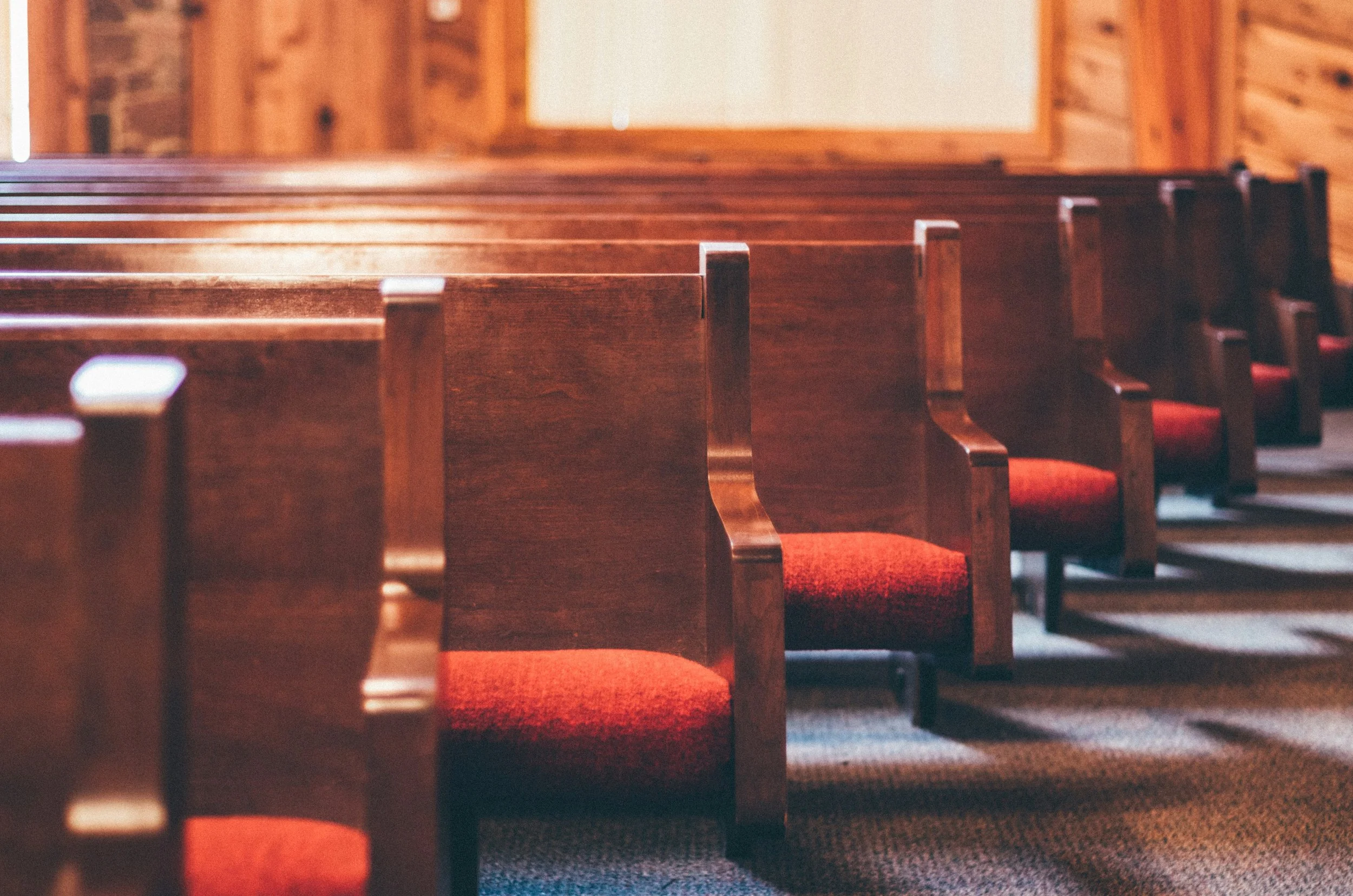 Wooden church pews with red cushions in a church interior.