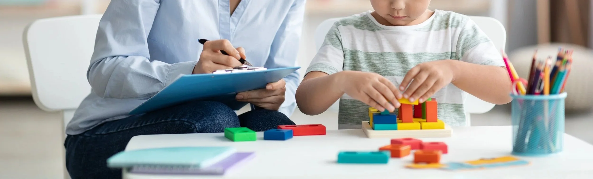 Child playing with colorful building blocks with adult observing and taking notes.
