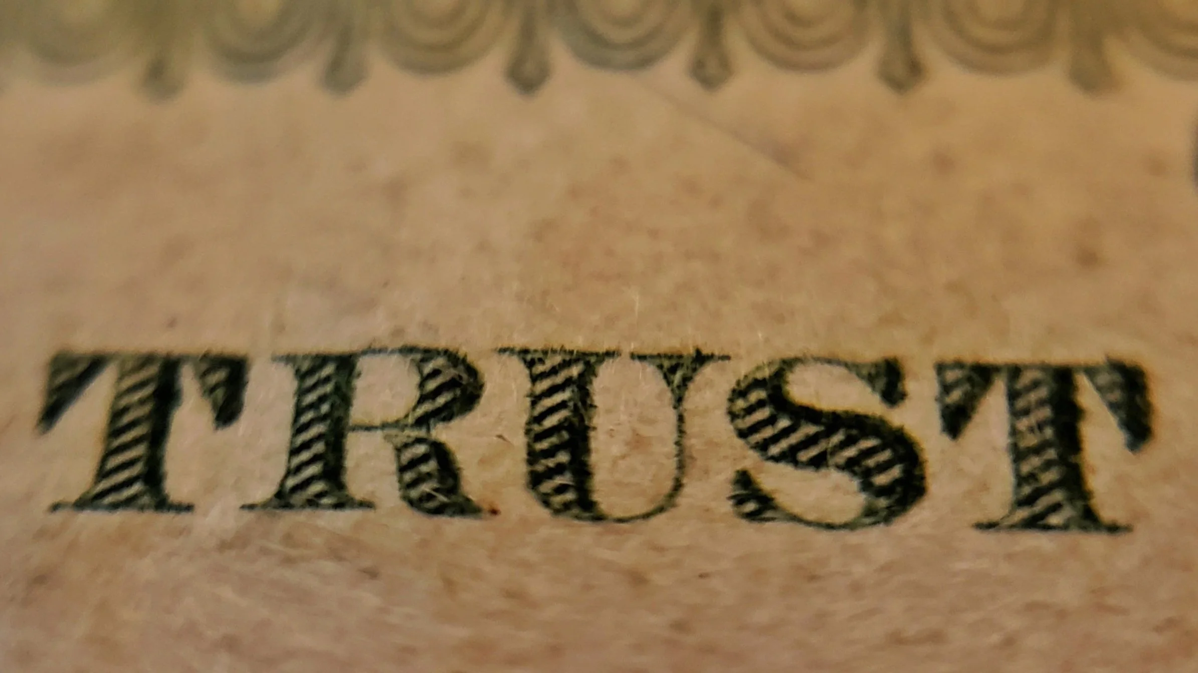Close-up of the word 'TRUST' printed in black, with a striped pattern, on brown paper.