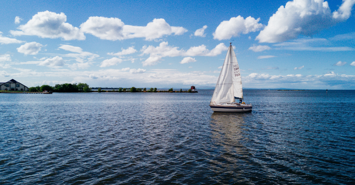 Een zeilboot op een groot meer met blauwe wateren onder een deels bewolkte hemel.