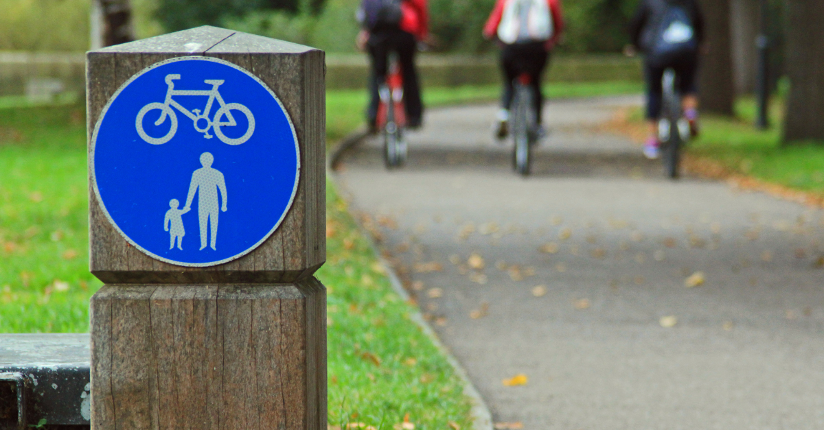 Fiets- en voetgangerspad met een blauw verkeersbord dat aangeeft dat het pad gedeeld wordt door fietsers en voetgangers, terwijl in de achtergrond vier mensen op fietsen rijden.