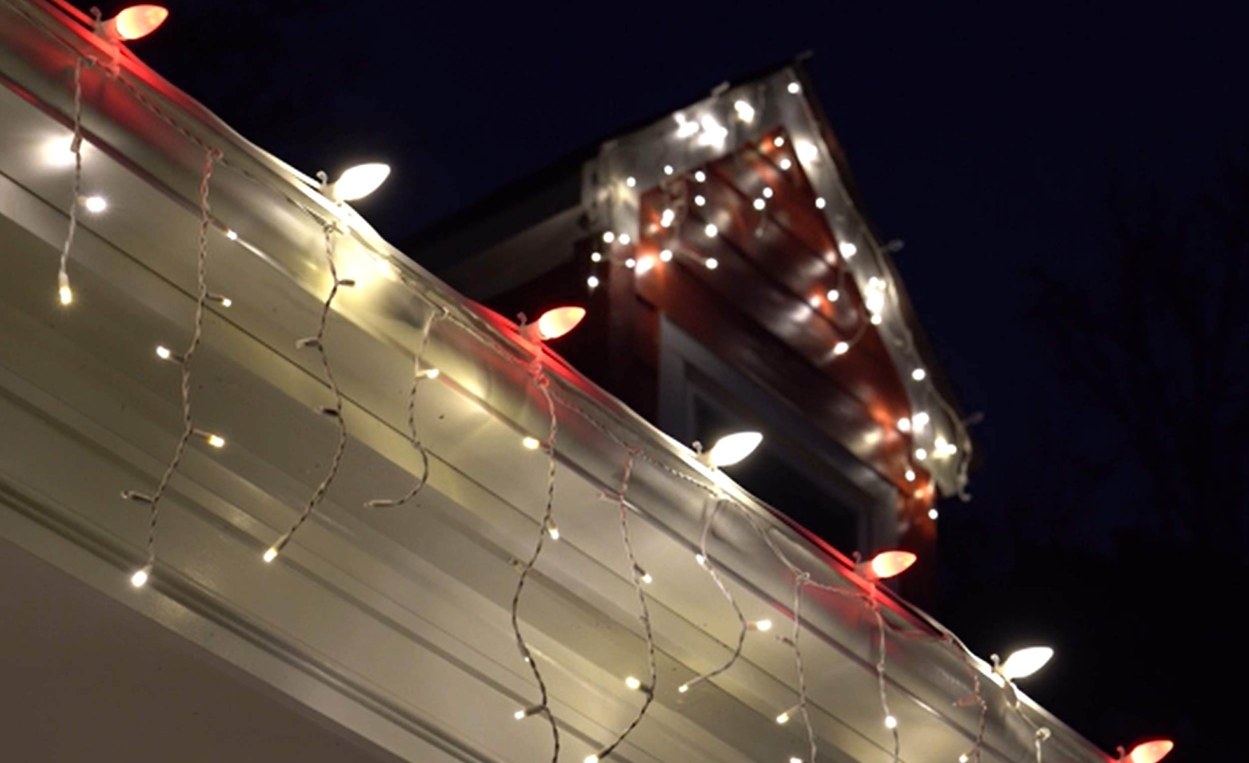 Close-up of a house's roofline decorated with white and red holiday string lights at night for Christmas lighting inspiration for Neon Noel customers in Lamar, Fannin, and Hunt County, Texas