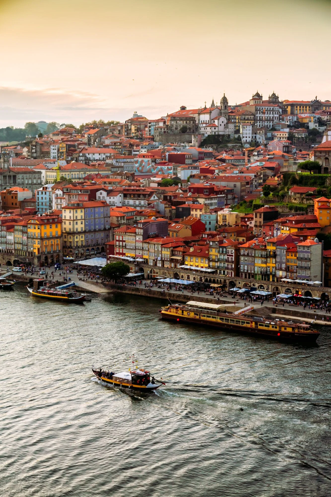 Fine art print photography for modern living room wall decor in Zürich.. A scenic view of a river with boats sailing past colorful buildings and a historic hillside town at sunset.