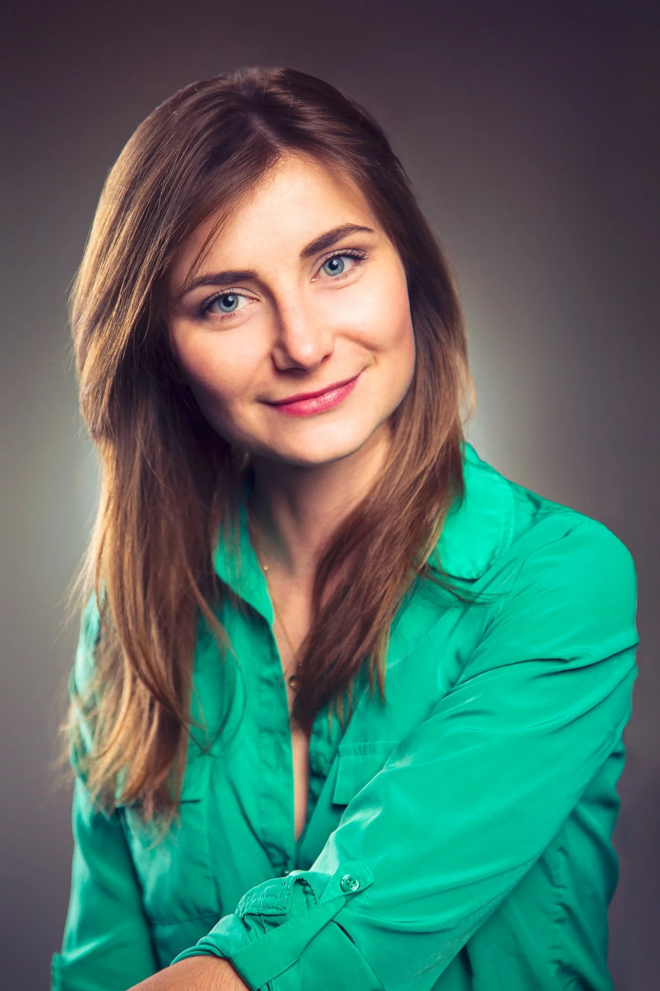 Portrait, Fitness & Commercial Photographer Zurich. A woman with long brown hair and blue eyes smiling at the camera, wearing a bright green satin blouse, against a gradient gray background.