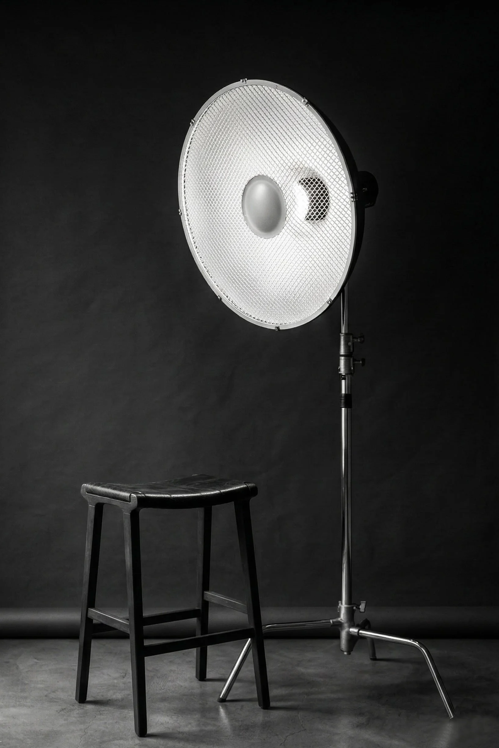 A photography studio with a black stool, a large studio light on a stand, and a dark background.
