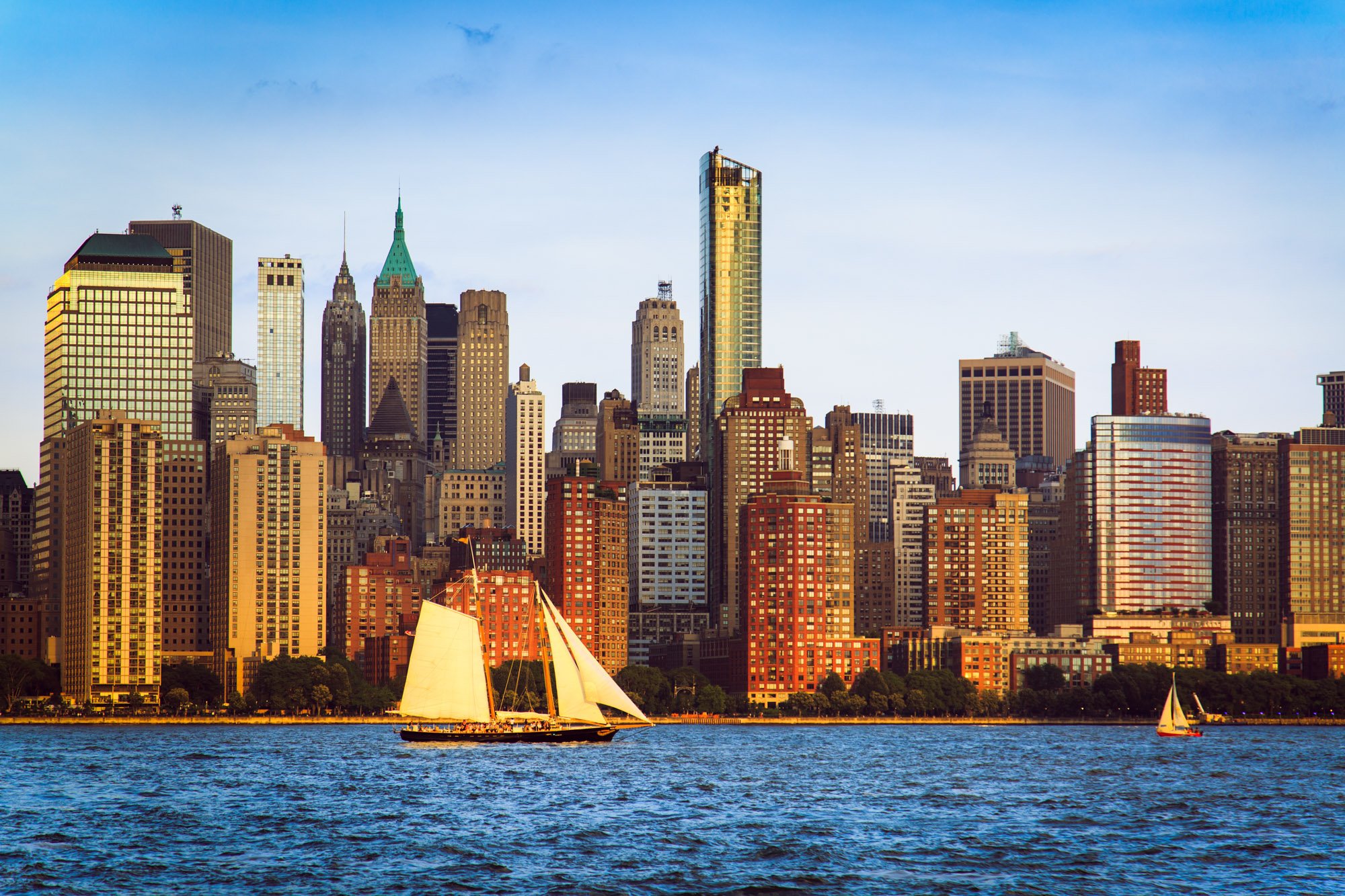 Fine art print photography for modern living room wall deFine art print photography for modern living room wall decor in Zürich. A city skyline with tall skyscrapers viewed from a body of water, with sailboats in the foreground and blue sky overhead.