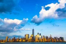 Skyline of a city during sunset with tall buildings and a partly cloudy sky.