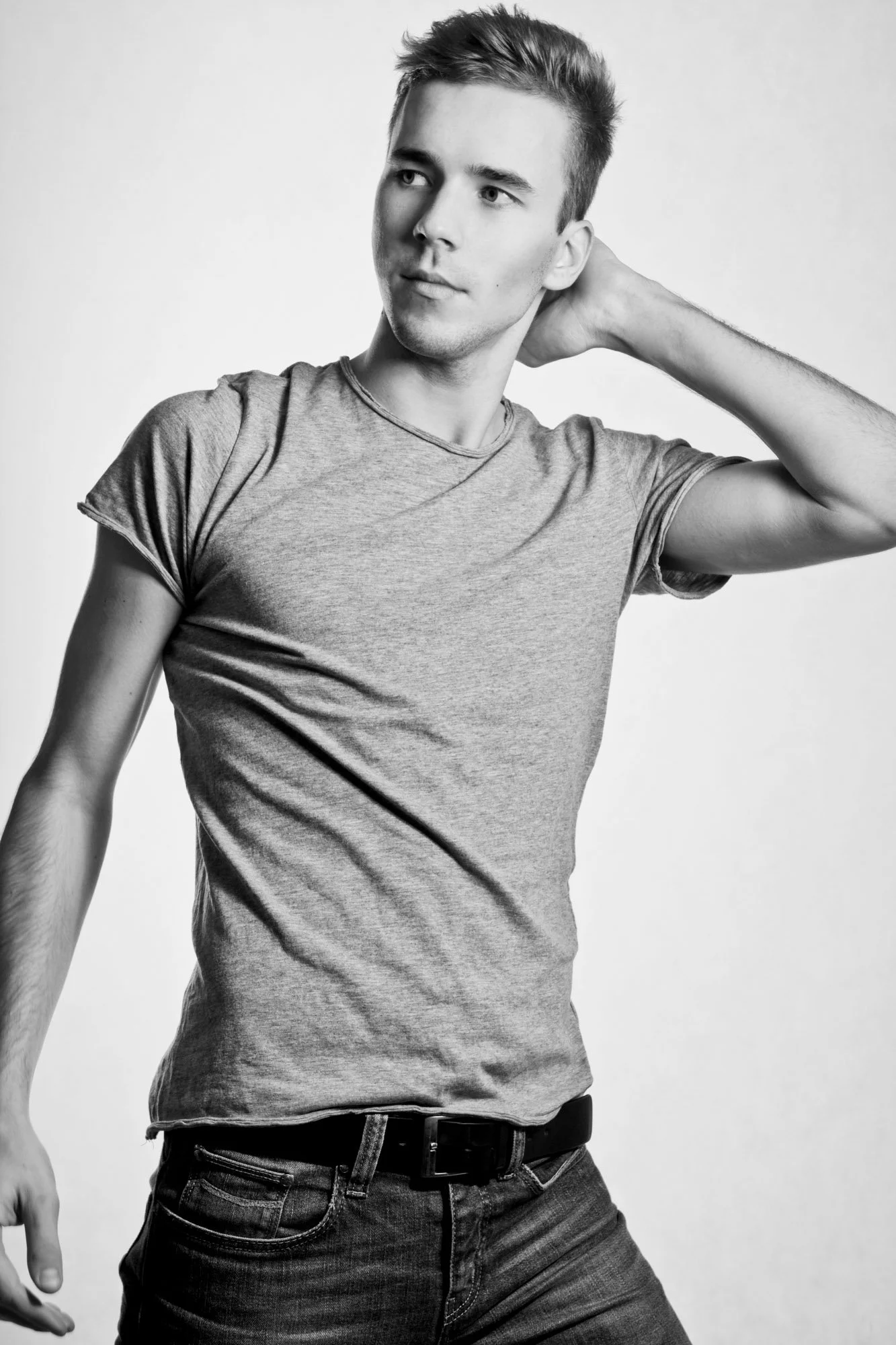 Portrait, Fitness & Commercial Photographer Zurich. A young man with short hair and casual clothing, posing with one hand behind his head, looking to the side, in a black and white studio portrait.