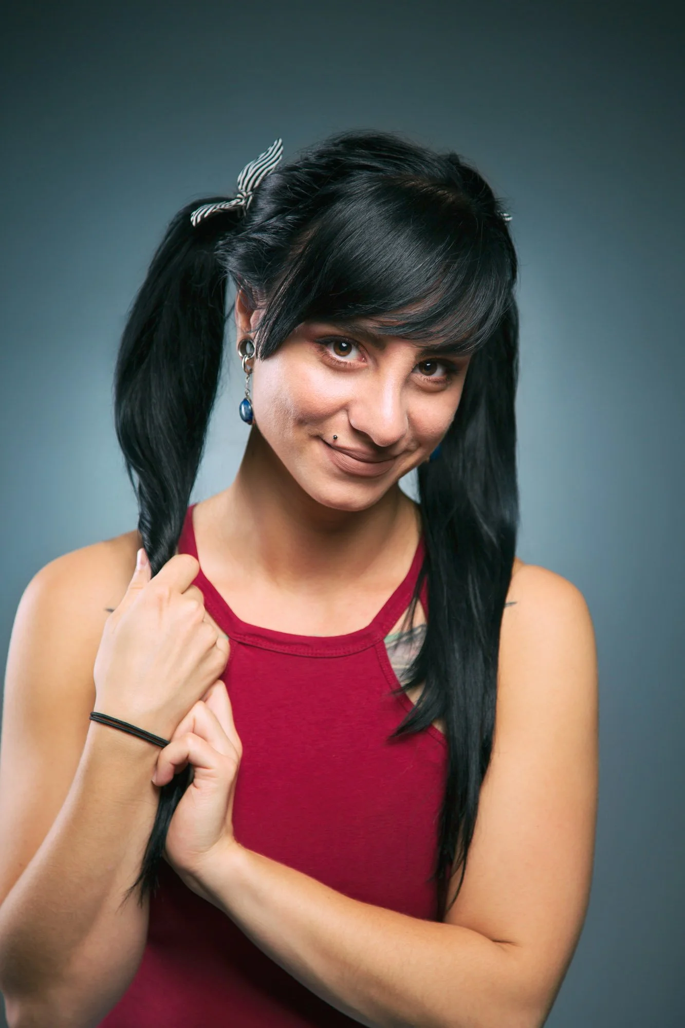 Portrait, Fitness & Commercial Photographer Zurich. Portrait of a woman with black hair in pigtails, wearing a red tank top, against a gray background.