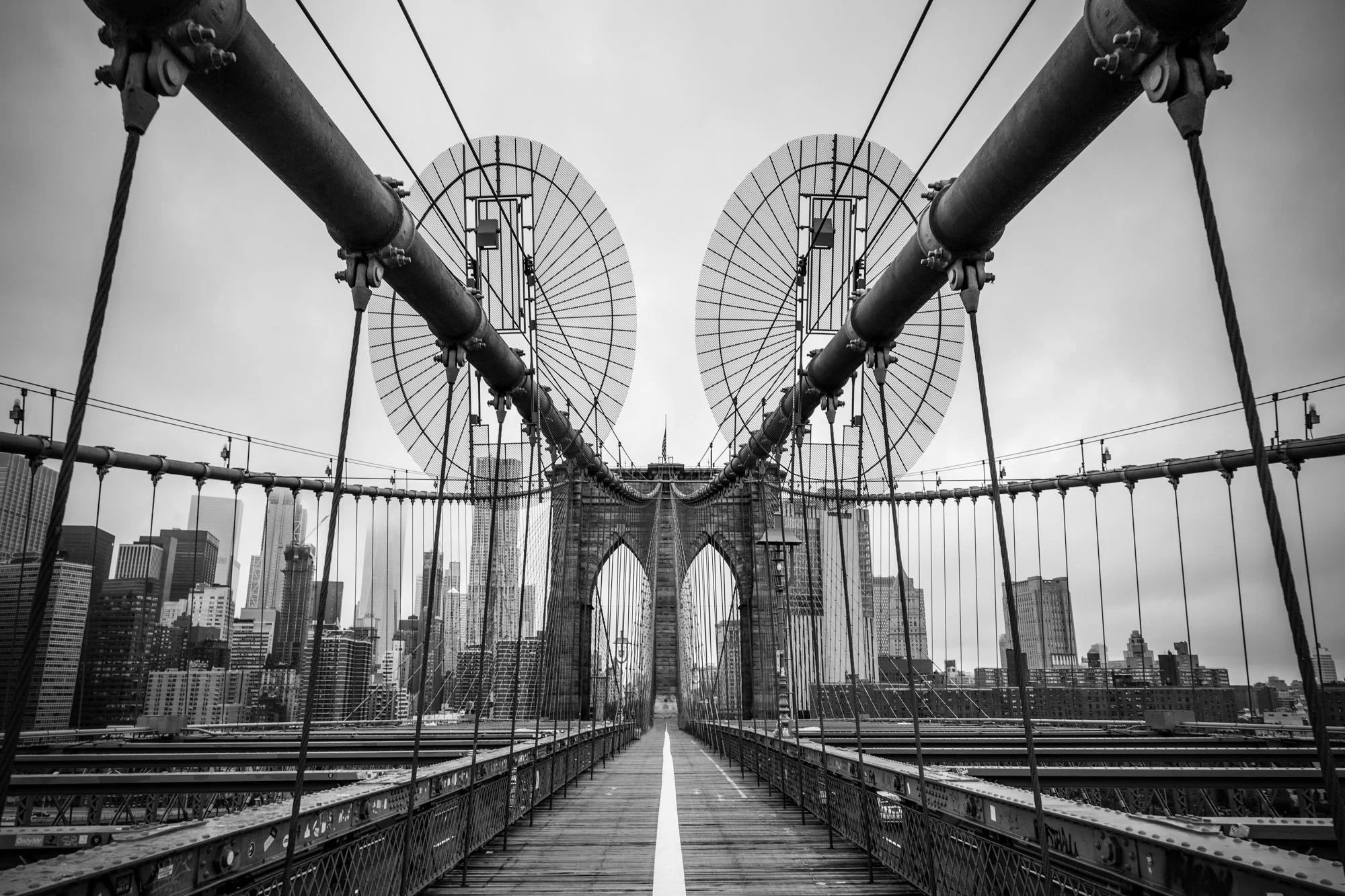 Black and white photo of the Brooklyn Bridge in New York City, showing the bridge's towers, cables, and city skyline in the background.