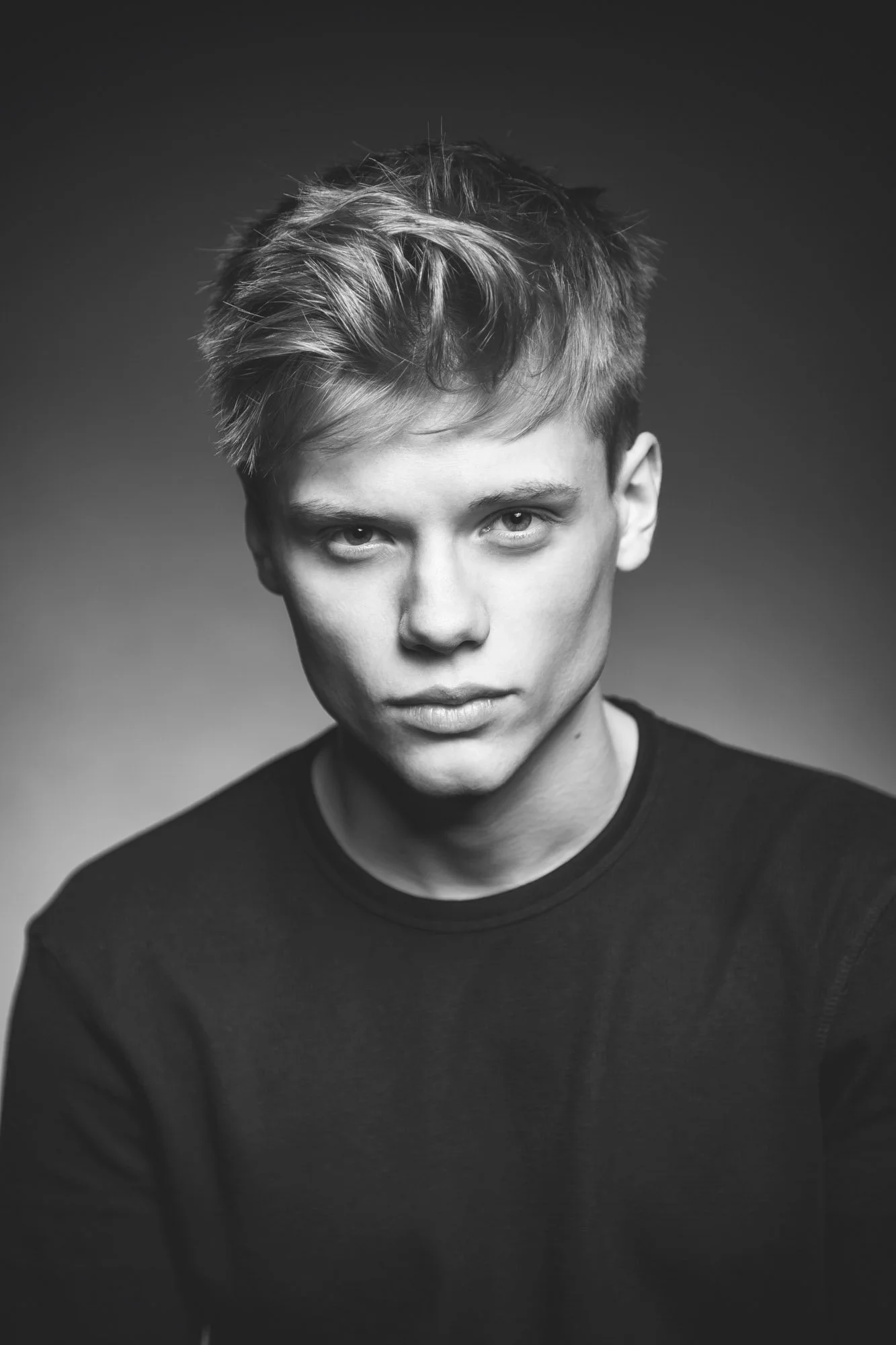 Portrait, Fitness & Commercial Photographer Zurich. Black and white portrait of a young man with short, tousled hair, looking directly at the camera with a serious expression, wearing a dark shirt.
