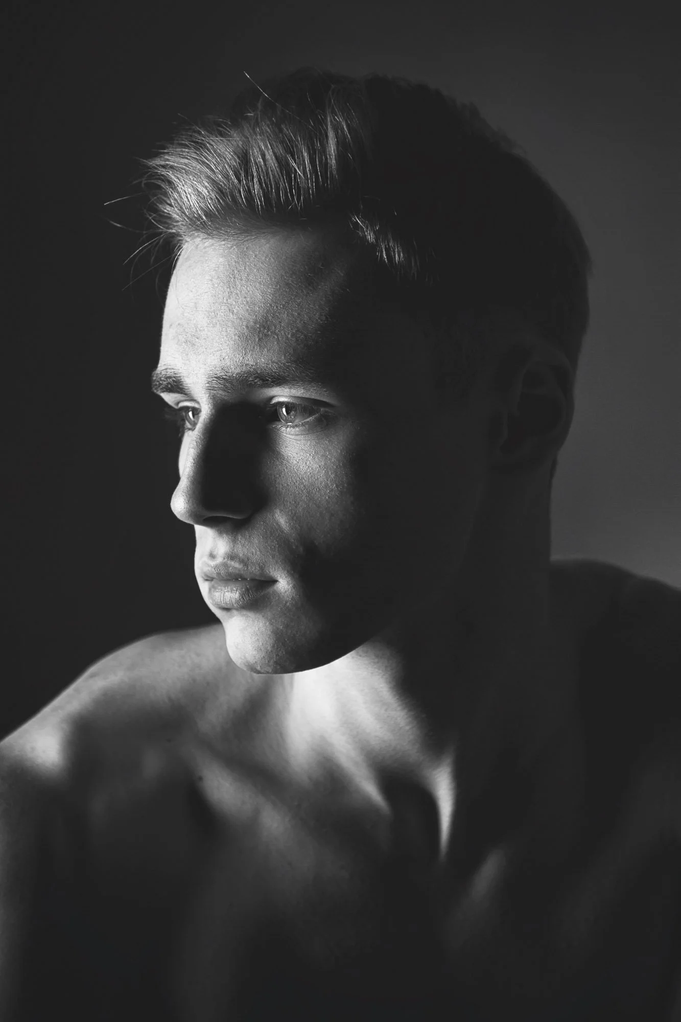 Portrait, Fitness & Commercial Photographer Zurich. A black and white portrait of a young man with short hair, looking to the side, with shadows creating a dramatic effect.