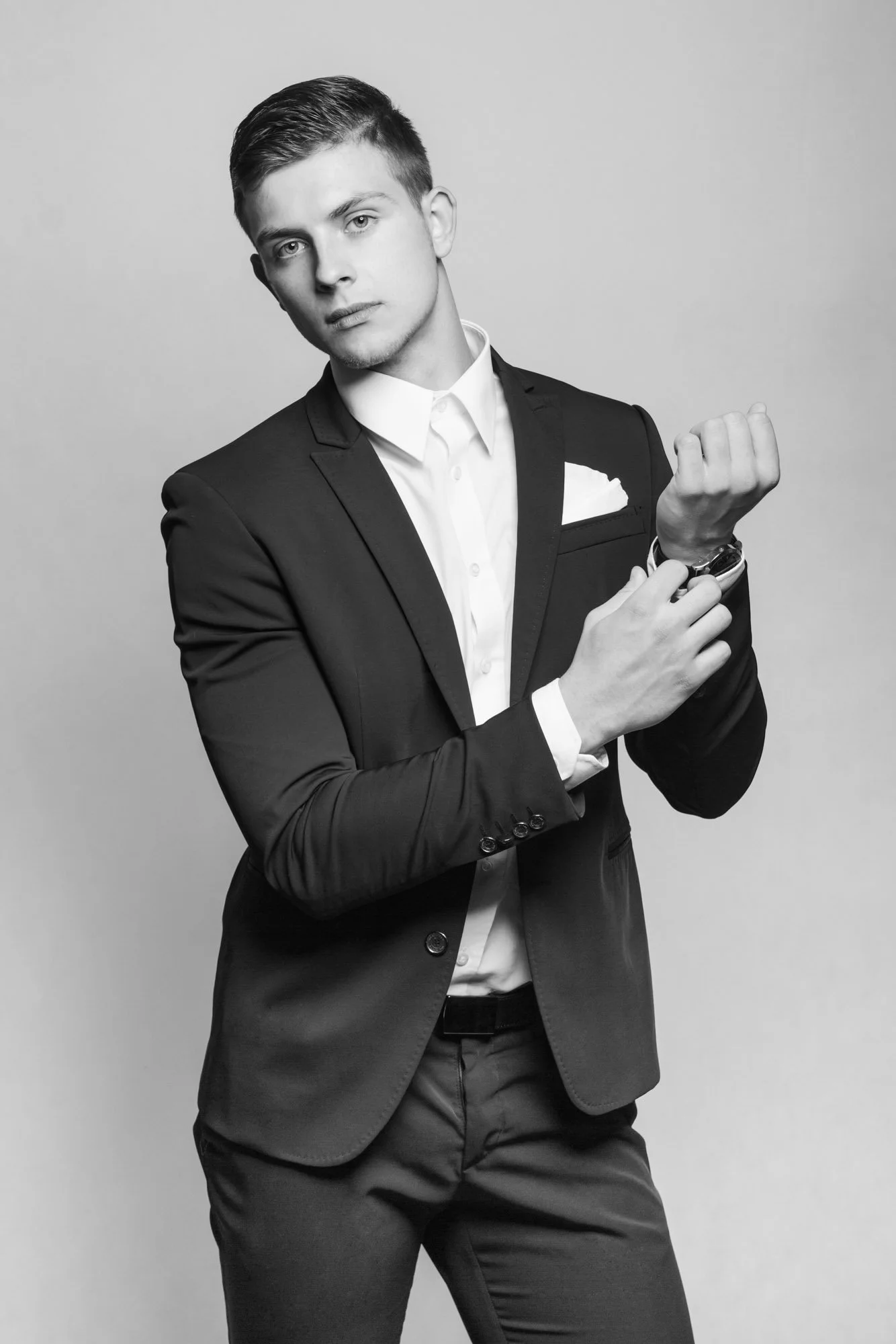 Portrait, Fitness & Commercial Photographer Zurich. Young man in a dark suit and white shirt adjusting his cuff in front of a plain background.
