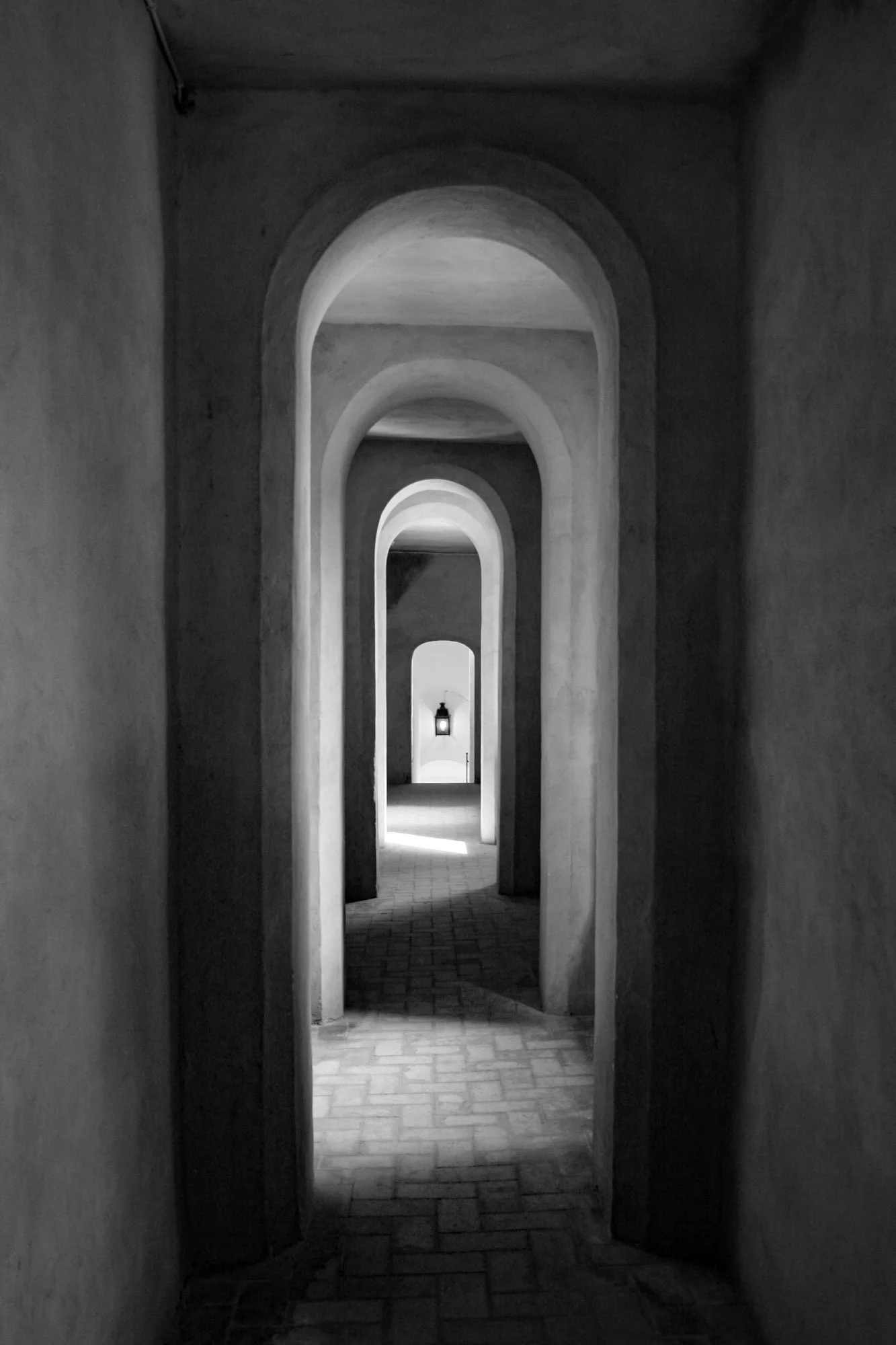 Fine art print photography for modern living room wall decor in Zürich.. A black and white photograph of a series of archways extending into the distance, with a light at the end illuminating the corridor.