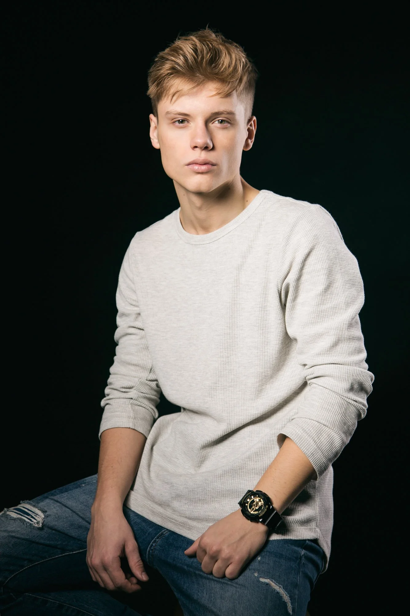 Portrait, Fitness & Commercial Photographer Zurich. Portrait of a young man with blond hair wearing a beige sweater and distressed jeans against a black background.