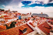 Rooftops of Lisbon with red tiles, historic buildings, and a cloudy sky.