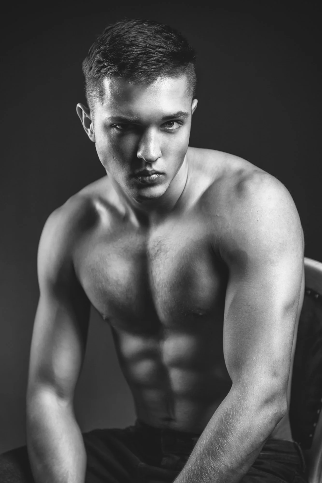 Portrait, Fitness & Commercial Photographer Zurich. Black and white photo of a shirtless young man with short hair, looking intently at the camera, with an intense expression, against a dark background.