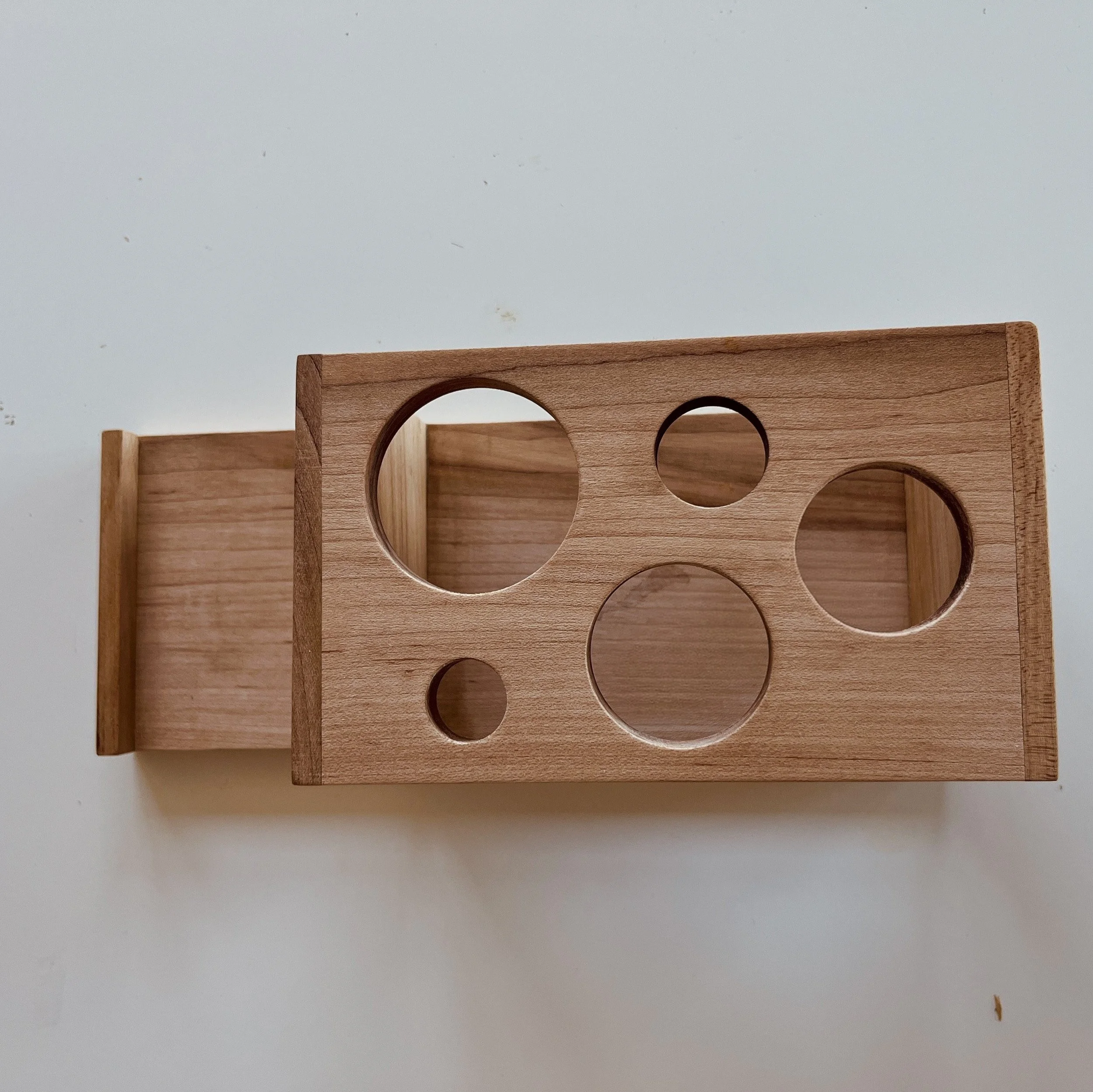 Wooden box with circular holes of various sizes, placed on a white surface.